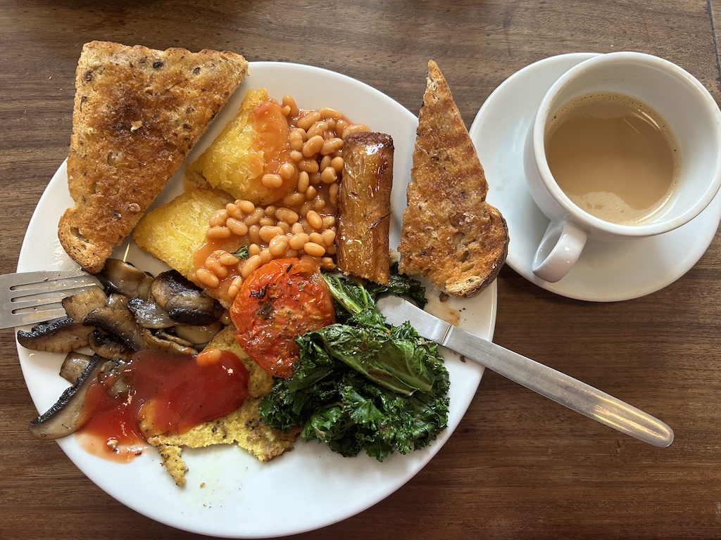 A fry up with toast, beans, hash browns, tomato, kale, mushrooms, sausage, tofu and a coffee.