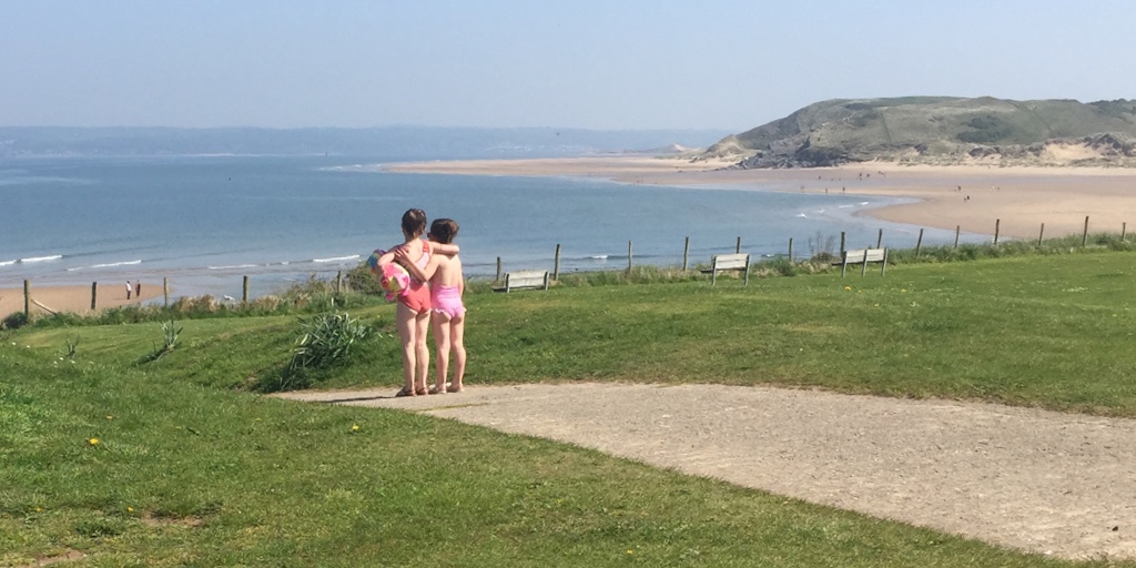 2 girls standing together, looking down at the beach on a sunny day