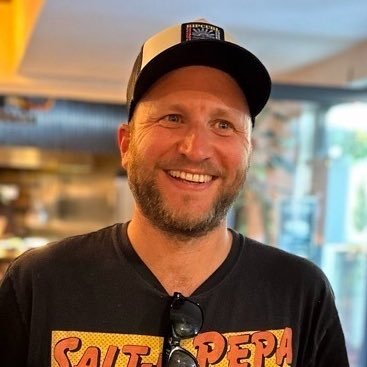 White man with a beard, wearing a baseball cap and smiling