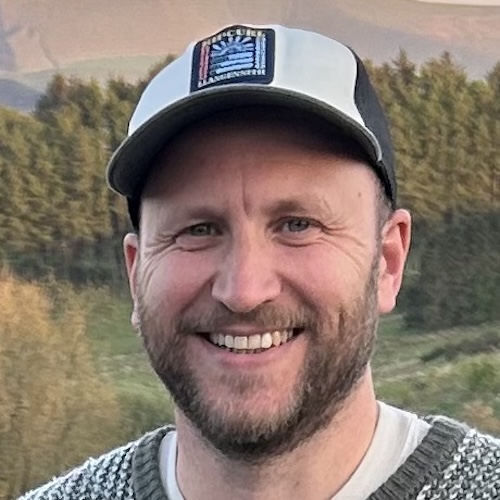 White man with a beard, wearing a baseball cap and smiling