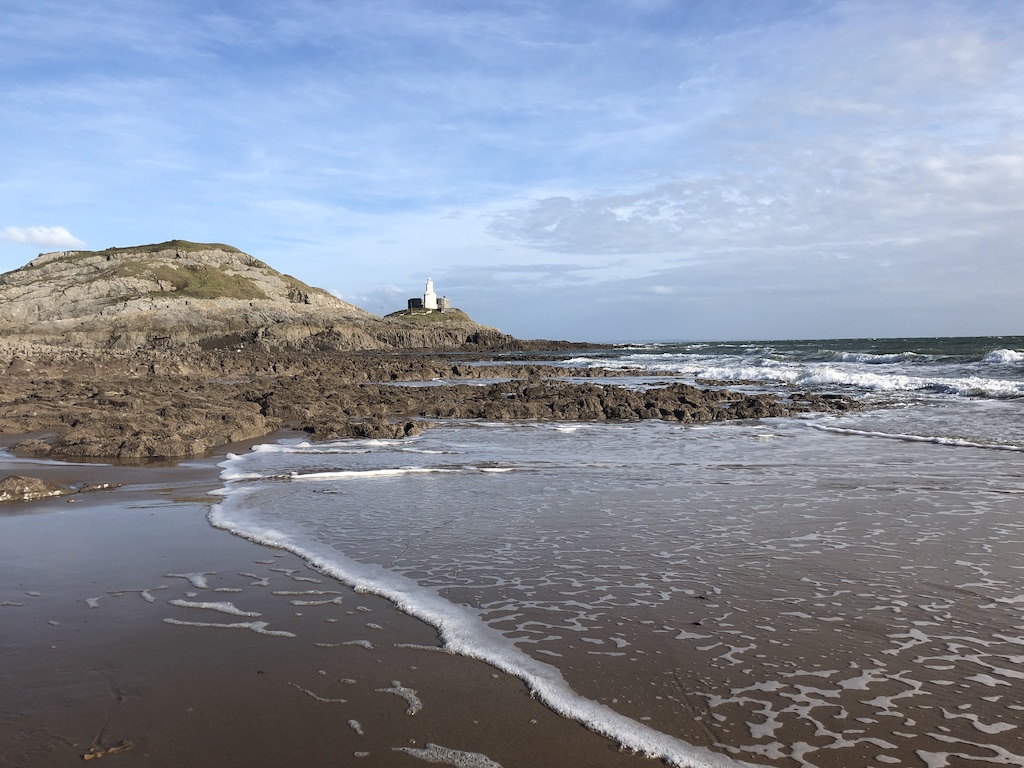 Sandy beach with rocks at the shore. In the distance is a lighthouse on a small rocky island.