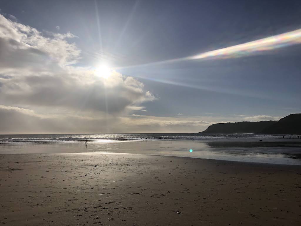 Beach with tide out. Sun, blue sky and cliffs in distance reflect off the water.