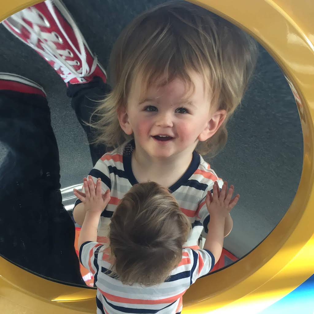A toddler looks at his distorted reflection in a round mirror.