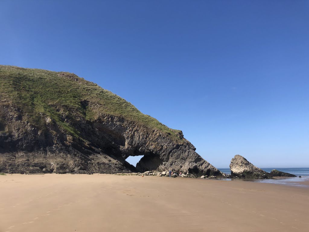 Rocky cliffs from the beach. A hole has formed in the rocks and you can see blue sky through the middle.