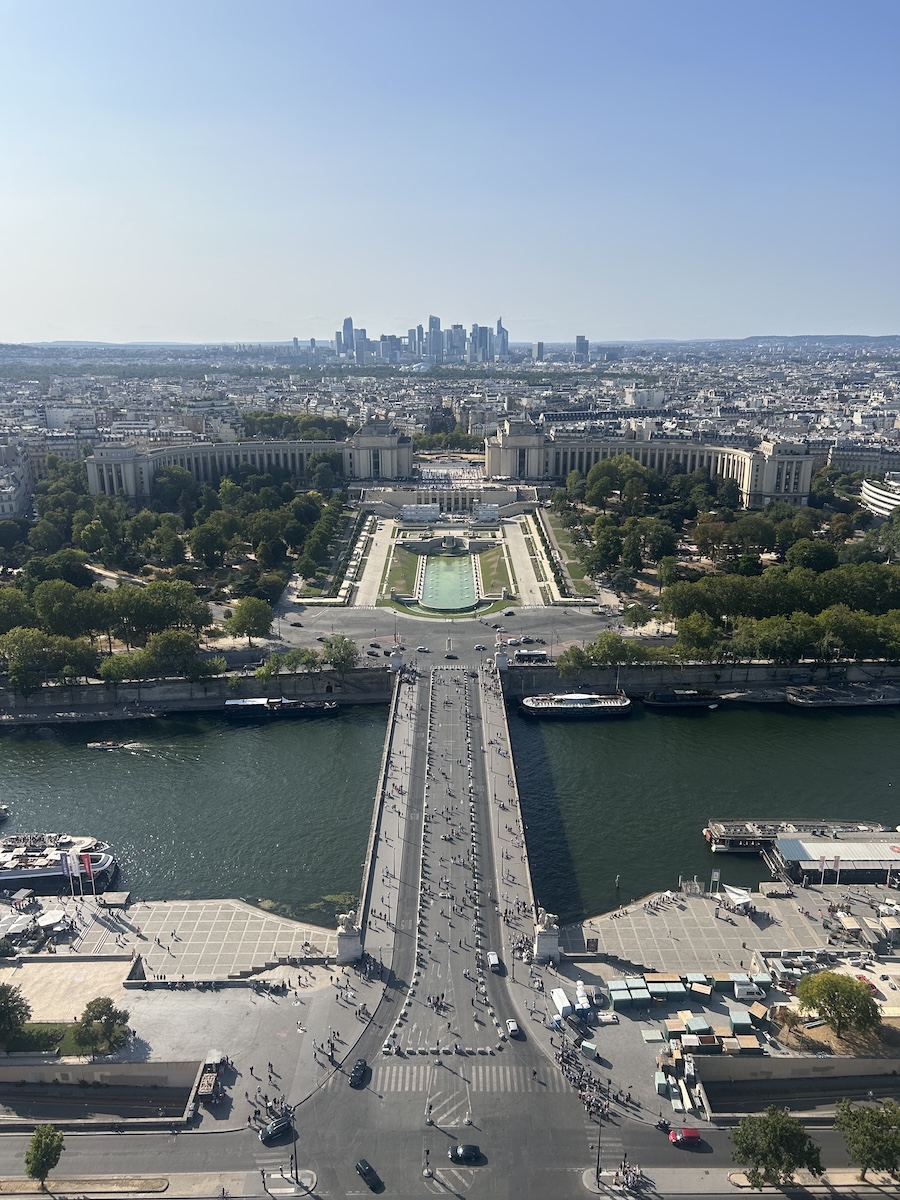 Looking down towards a busy bridge full of people, the road leads to a sprawling city in the distance.